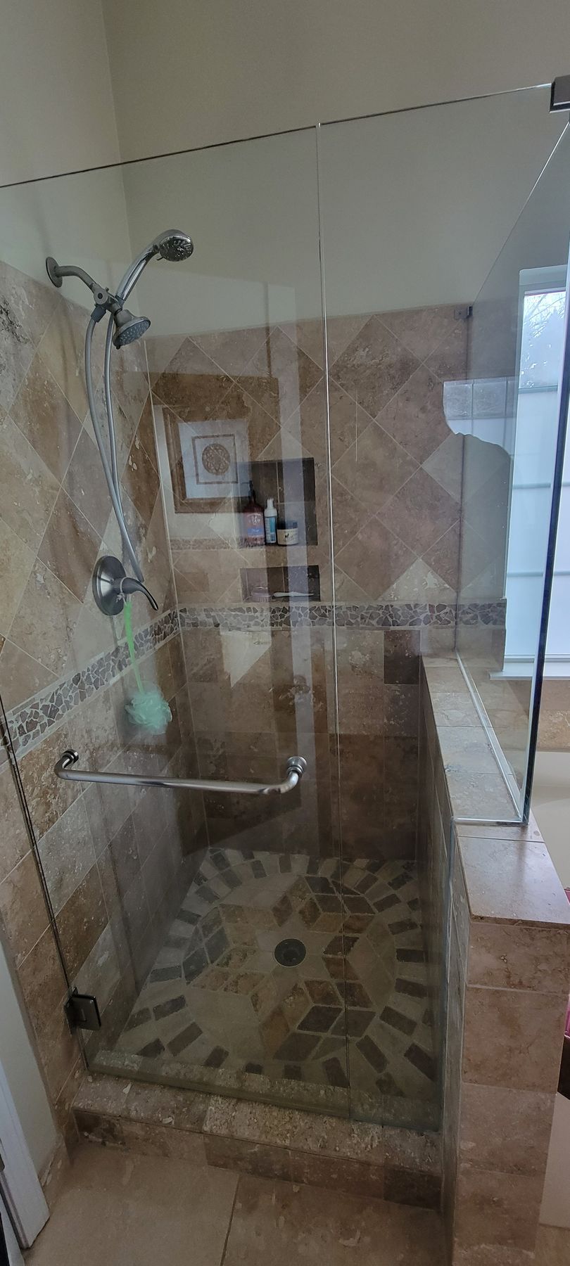 Glass-enclosed tiled shower with chrome fixtures and mosaic floor in a bathroom