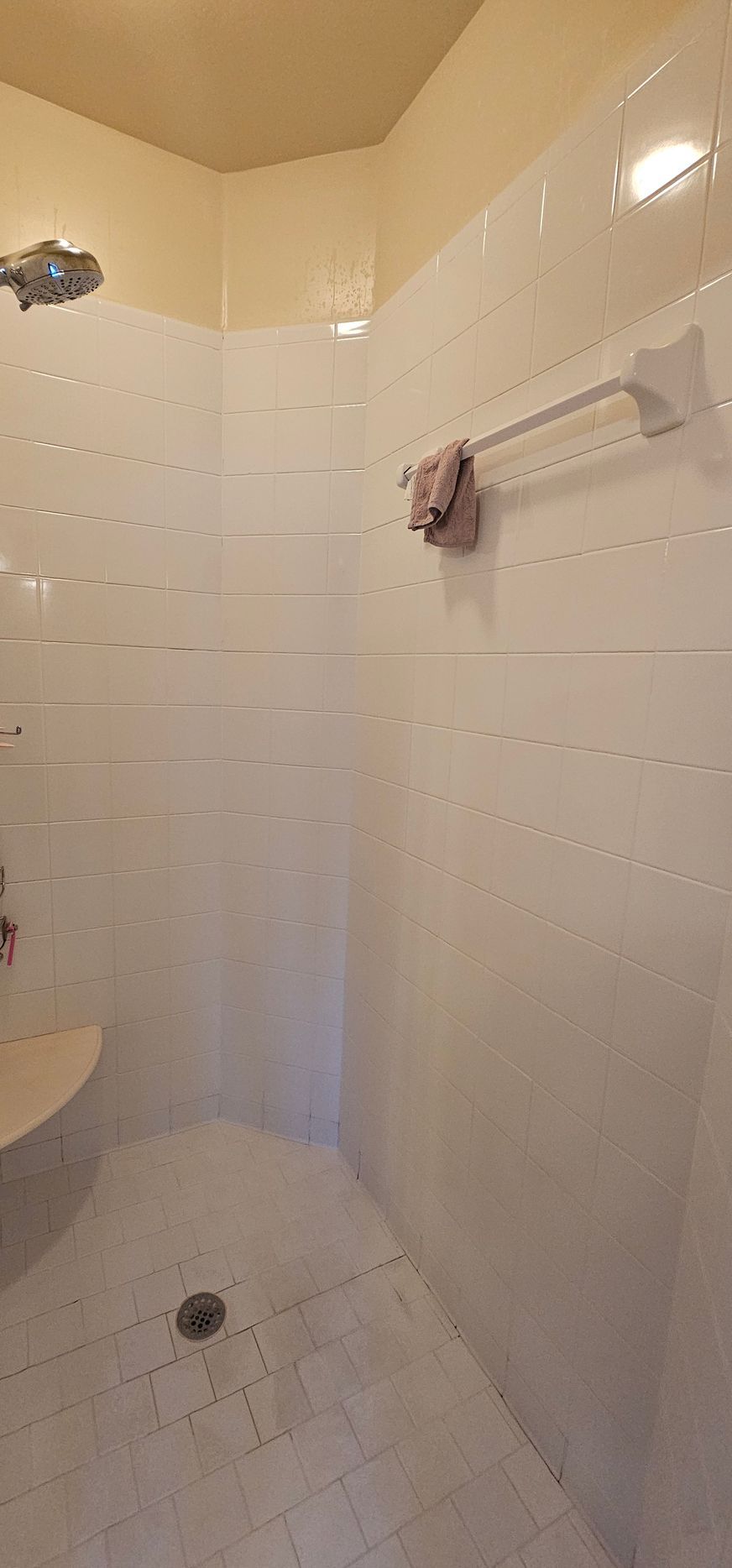 Small white-tiled shower stall with beige walls, chrome fixtures, and a towel on the rail.