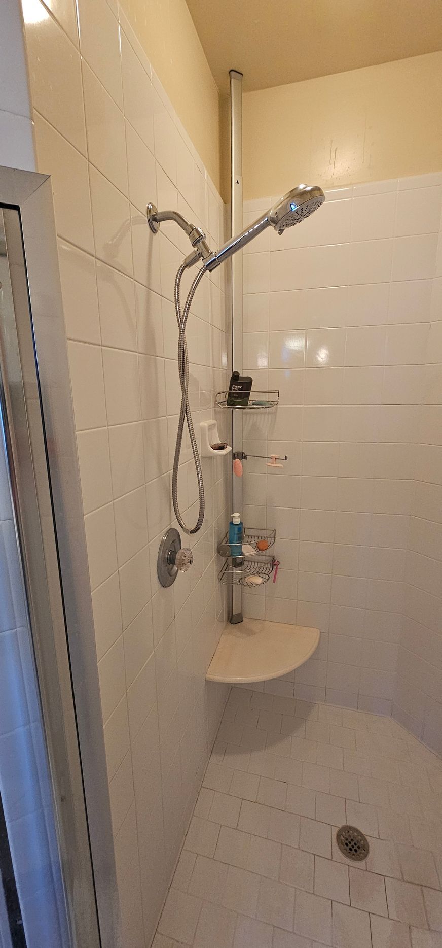 Small tiled bathroom with a wall-mounted shower, handheld sprayer, and a narrow pedestal sink.
