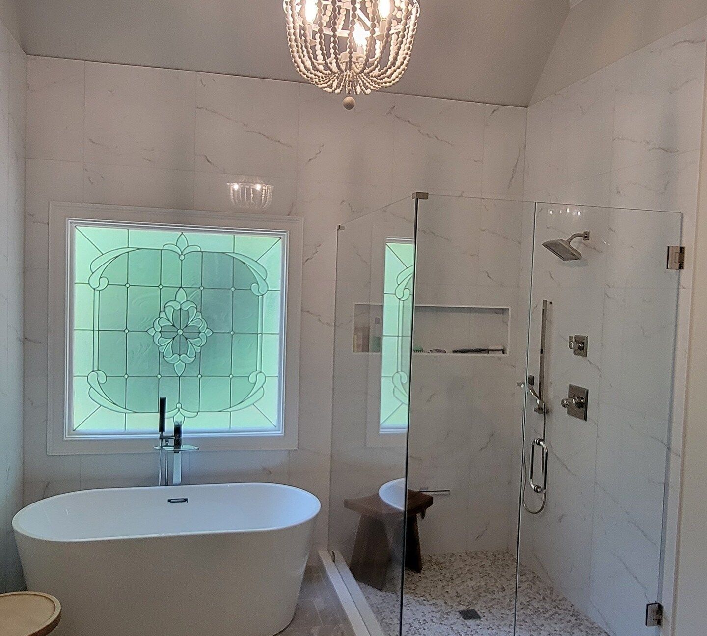 Modern white bathroom with a freestanding tub, glass shower, and turquoise stained-glass windows.