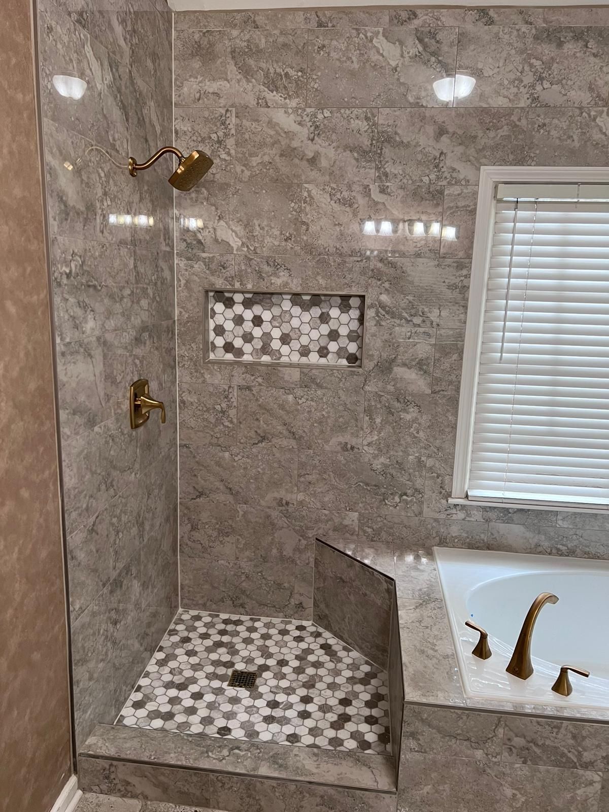 Bathroom with tiled walk-in shower, built-in bench, window blinds, and adjacent tub faucet.
