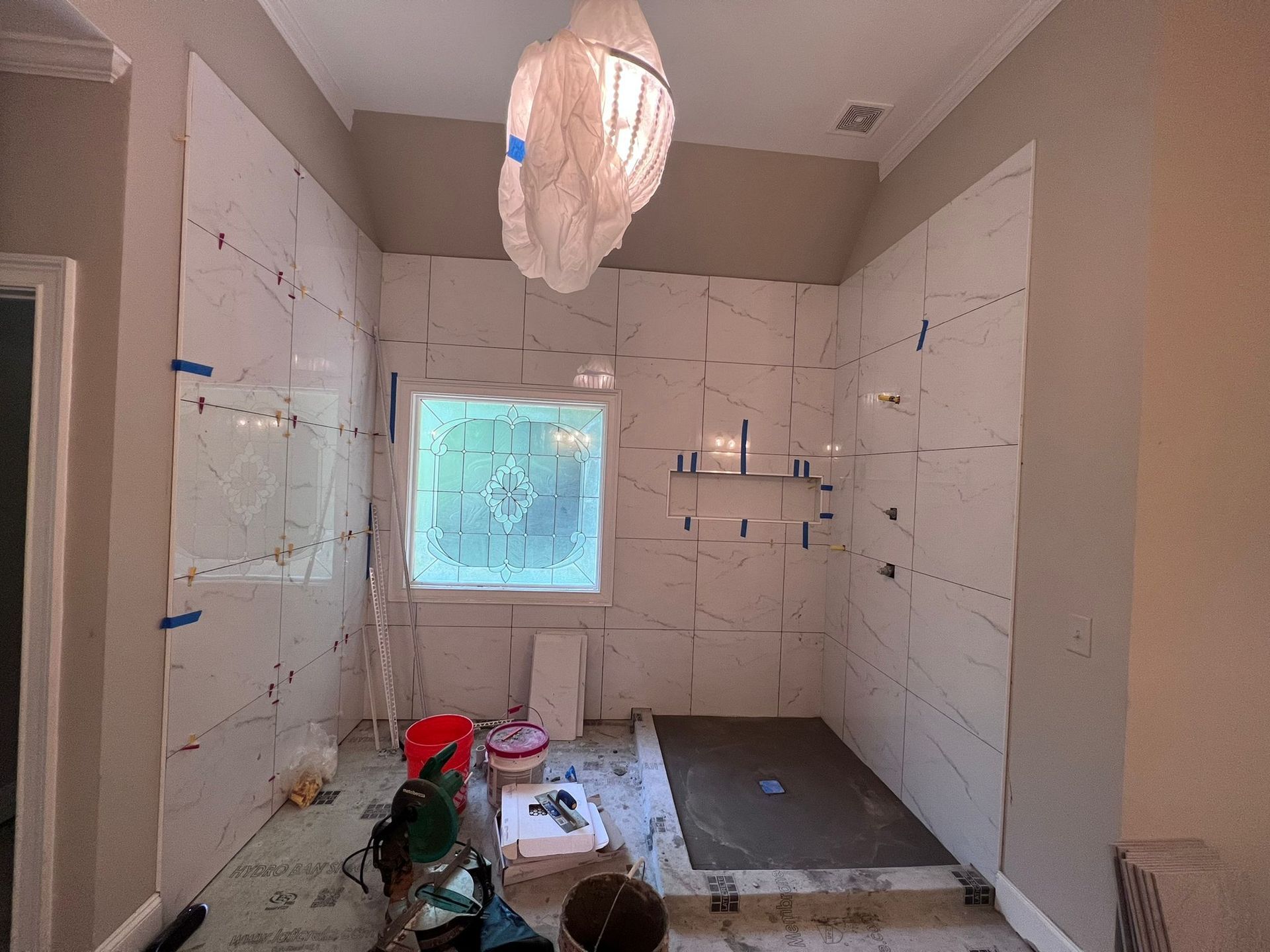 Bathroom under renovation with white tiled walls, window light, and tools on the floor