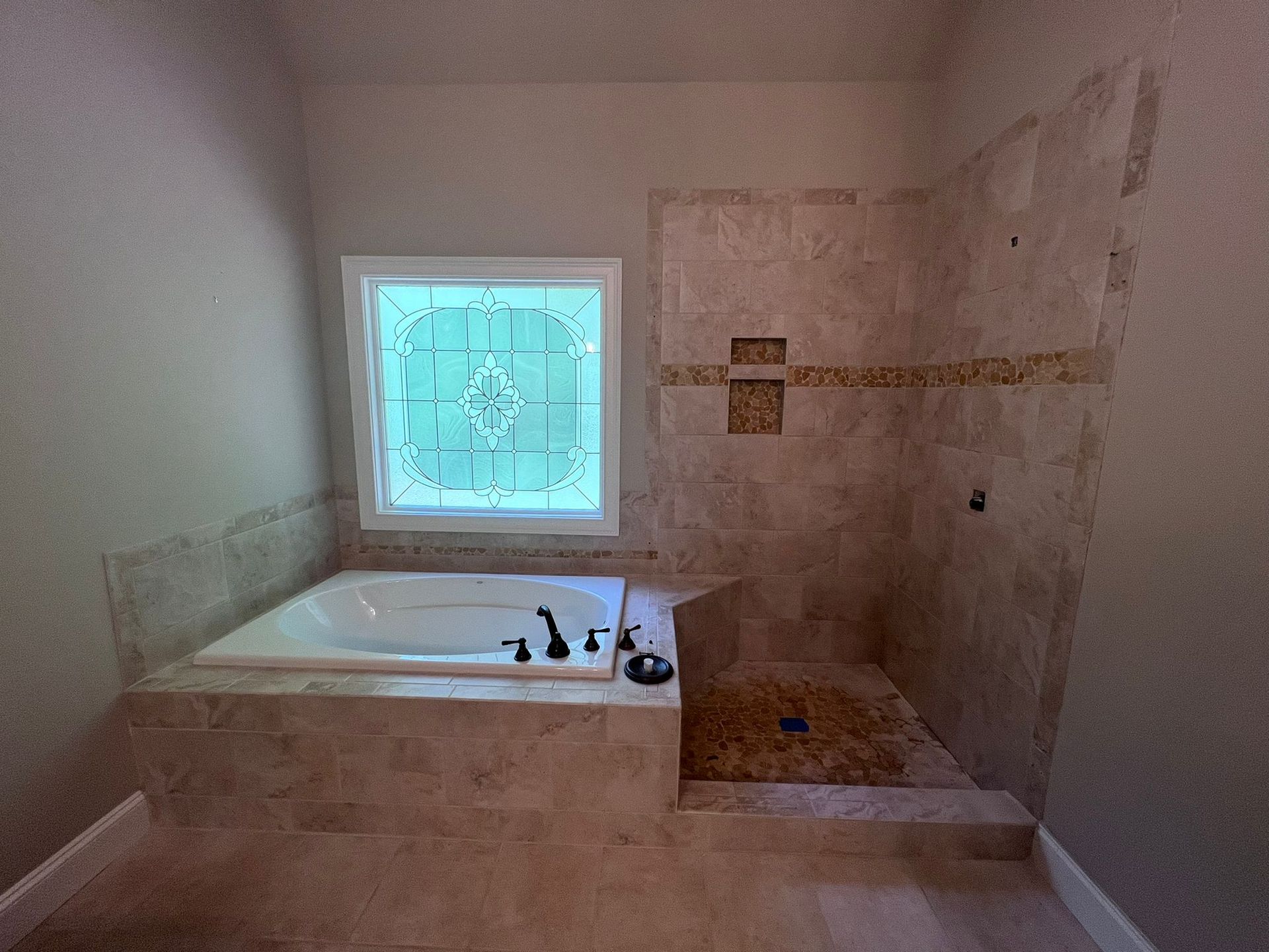 Bathroom with a built-in bathtub, walk-in shower, and frosted window on tiled walls.