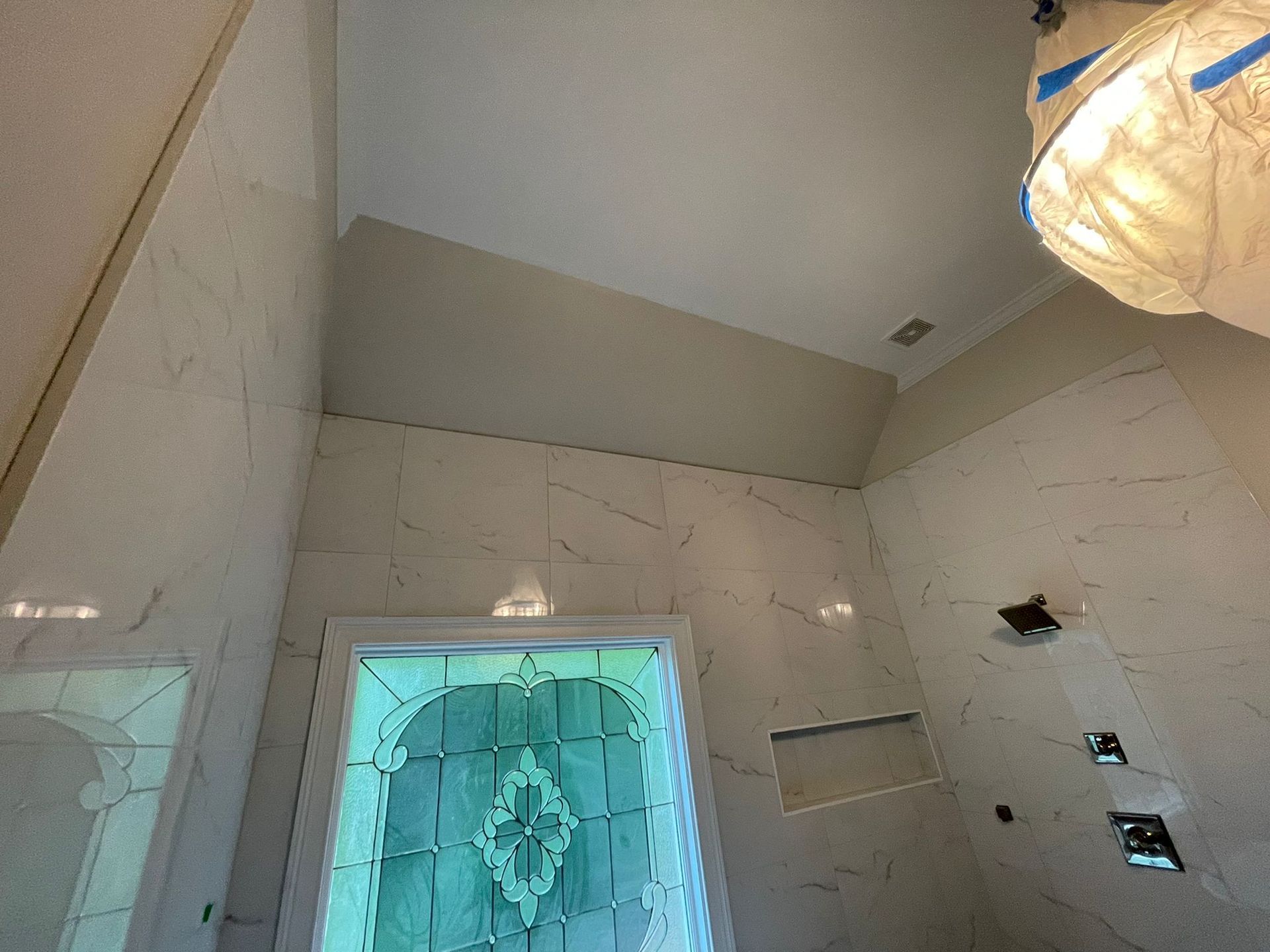 White tiled bathroom ceiling and walls with a frosted glass shower door and hanging light fixture.