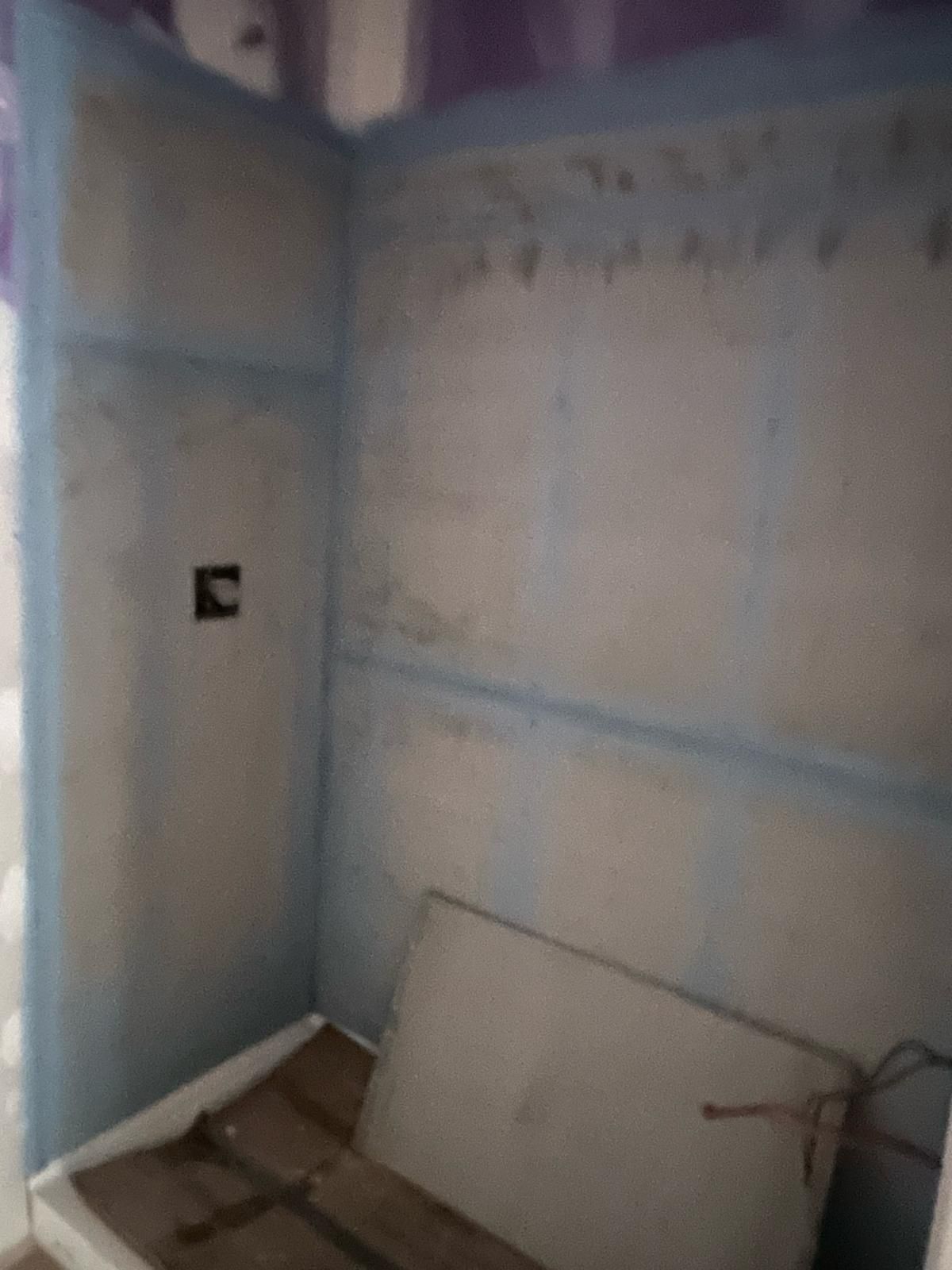 Unfinished room corner with blue drywall, a wall outlet, and a board leaning against the floor.