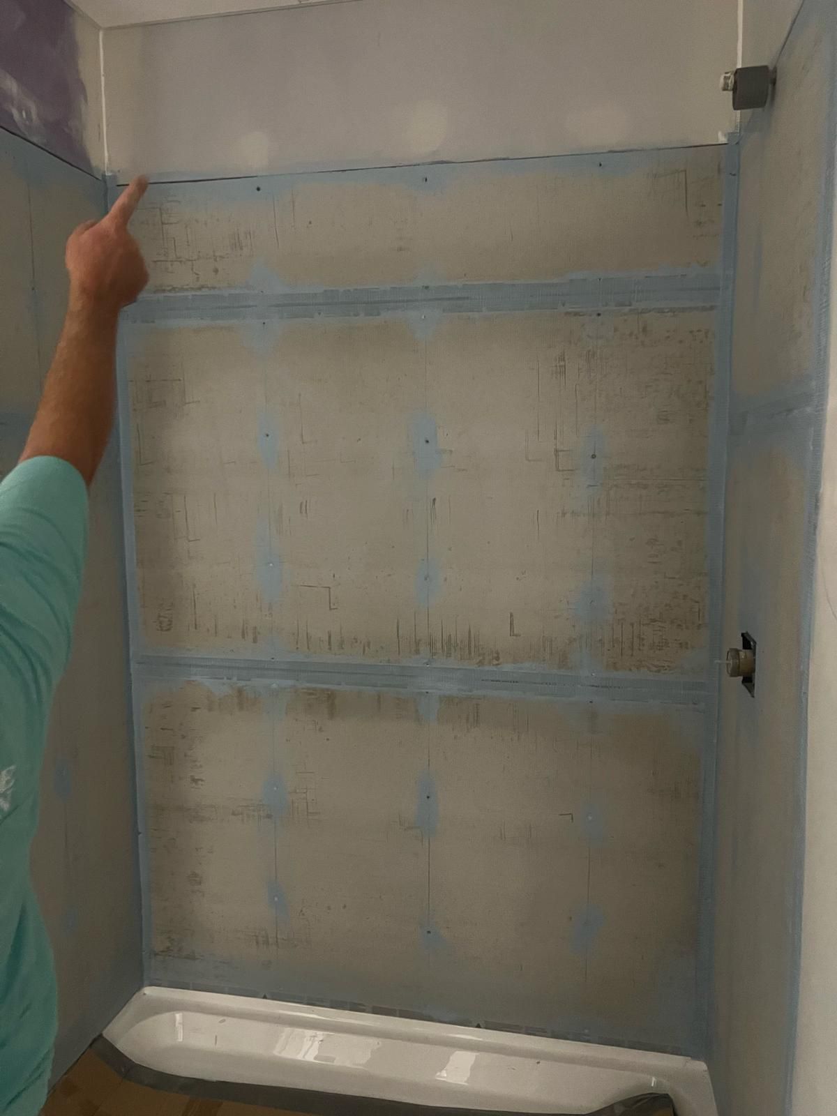 Person measuring a tiled shower wall with a long level and tape measure