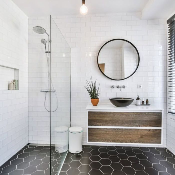 Modern white bathroom with hex tile floor, walk-in shower, round mirror, and wood vanity with black sink