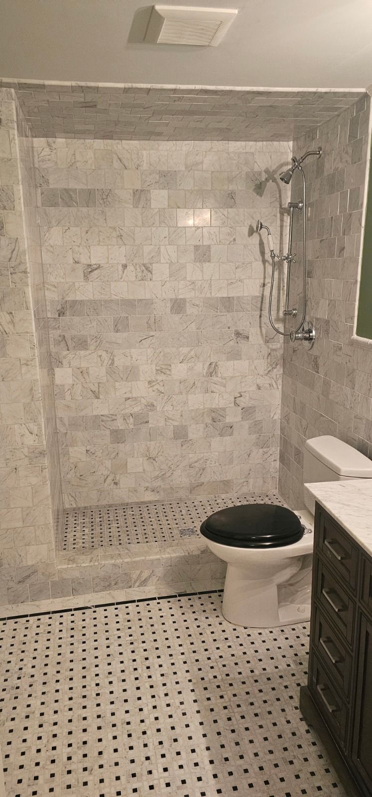 Small tiled bathroom with a shower, toilet, and vanity in neutral gray tones.