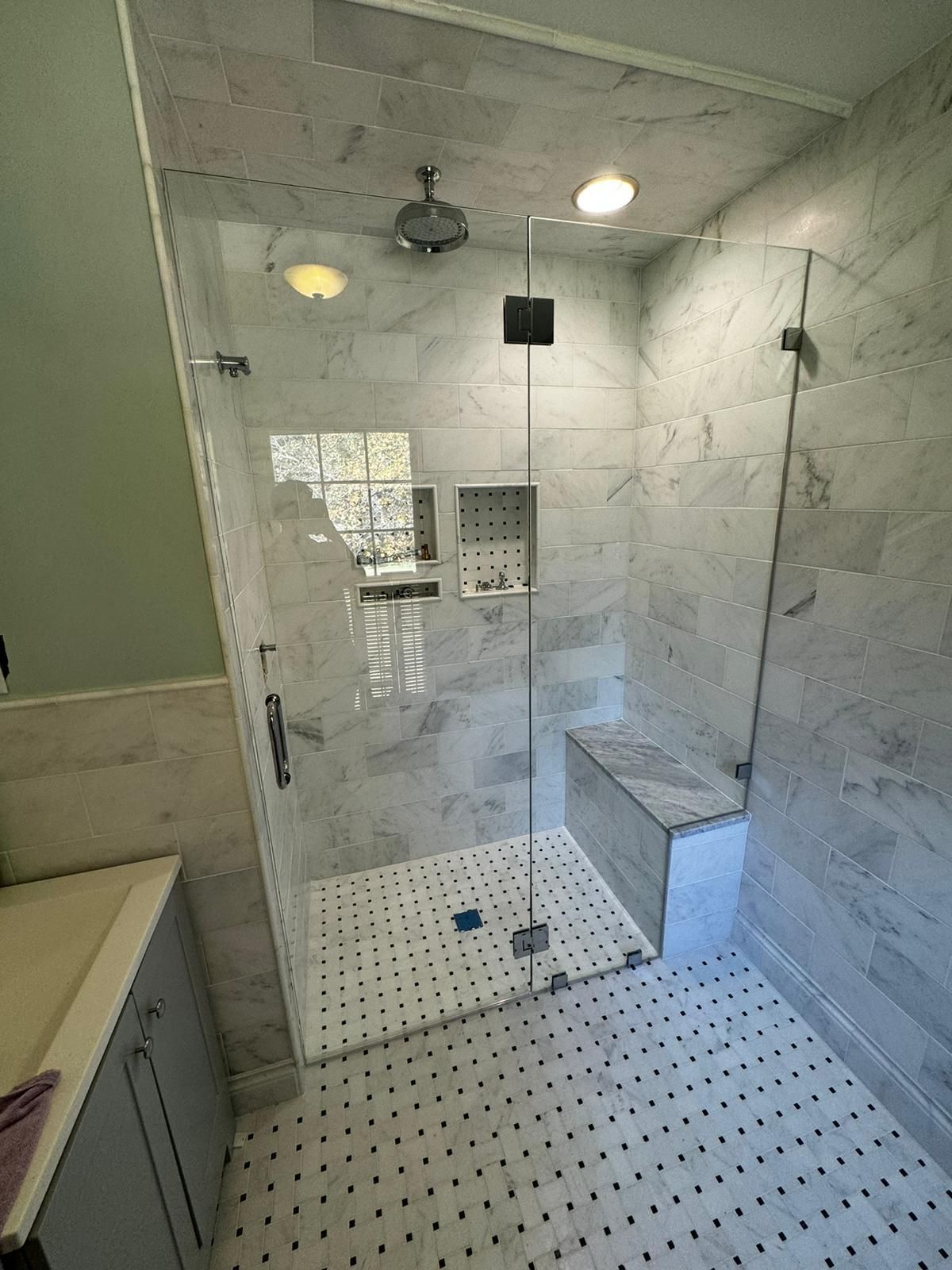 Walk-in shower with glass door, white tile walls, built-in bench, and small mosaic-tile floor.