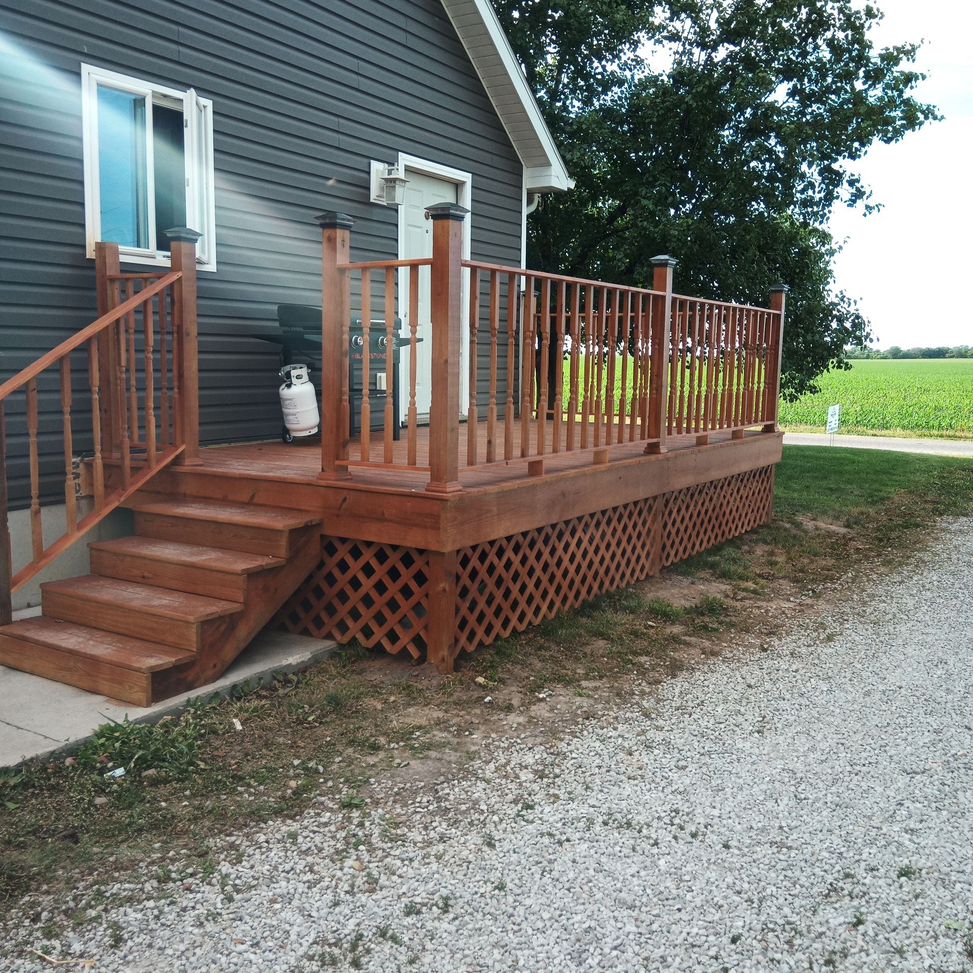 Wooden deck with stairs, railing, and lattice skirting, attached to a gray house.