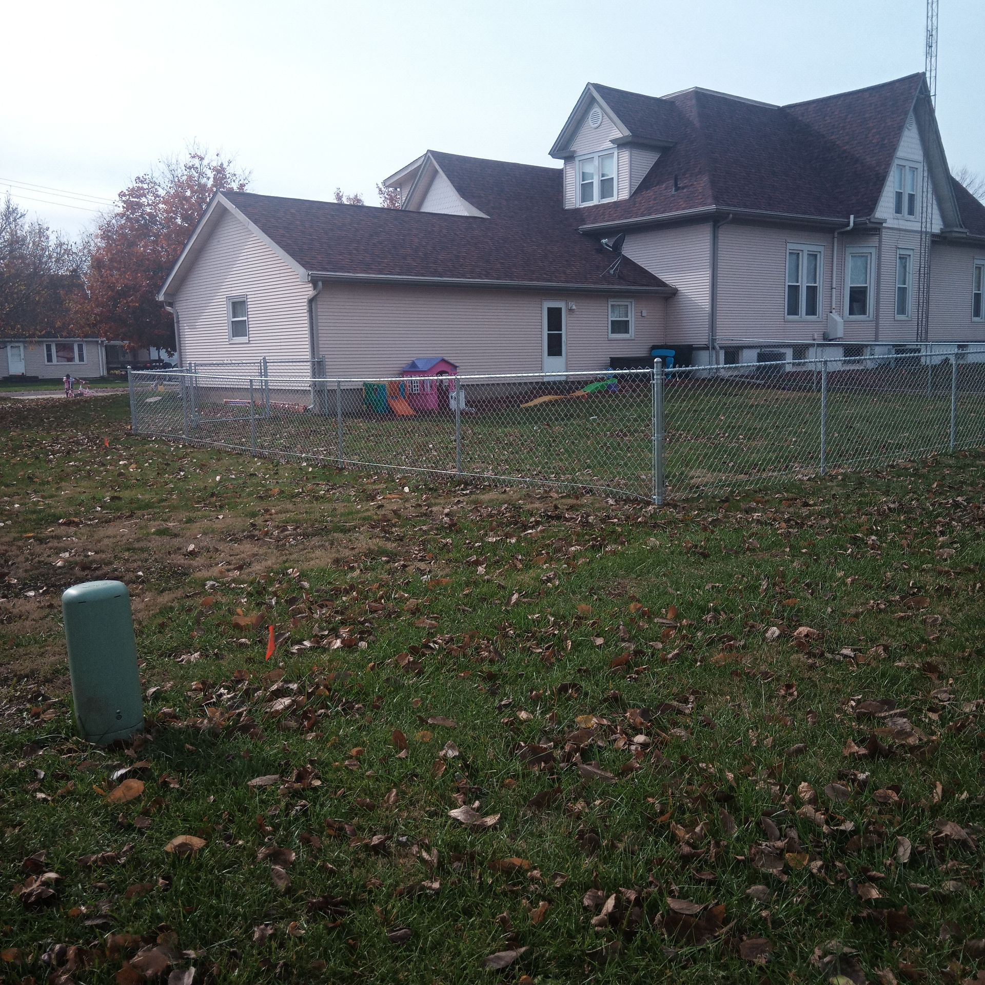 House with light siding, a dark roof, and a fenced-in yard, overcast sky.