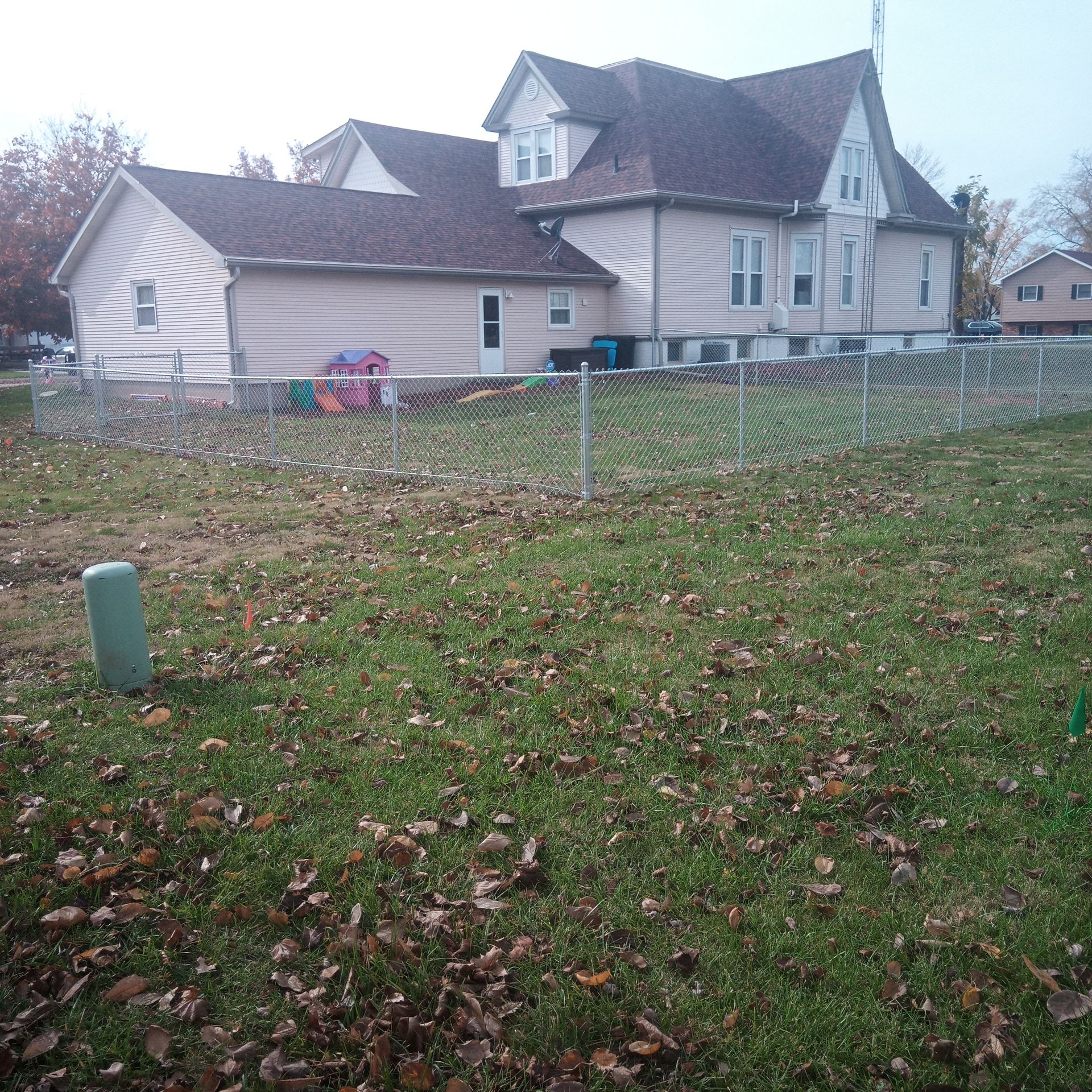 Large light-colored house with a chain-link fence in front, overcast sky, grass lawn.