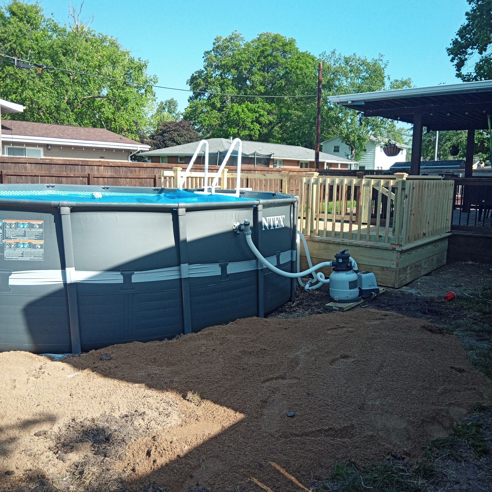 Above-ground pool with attached wooden deck in a backyard.