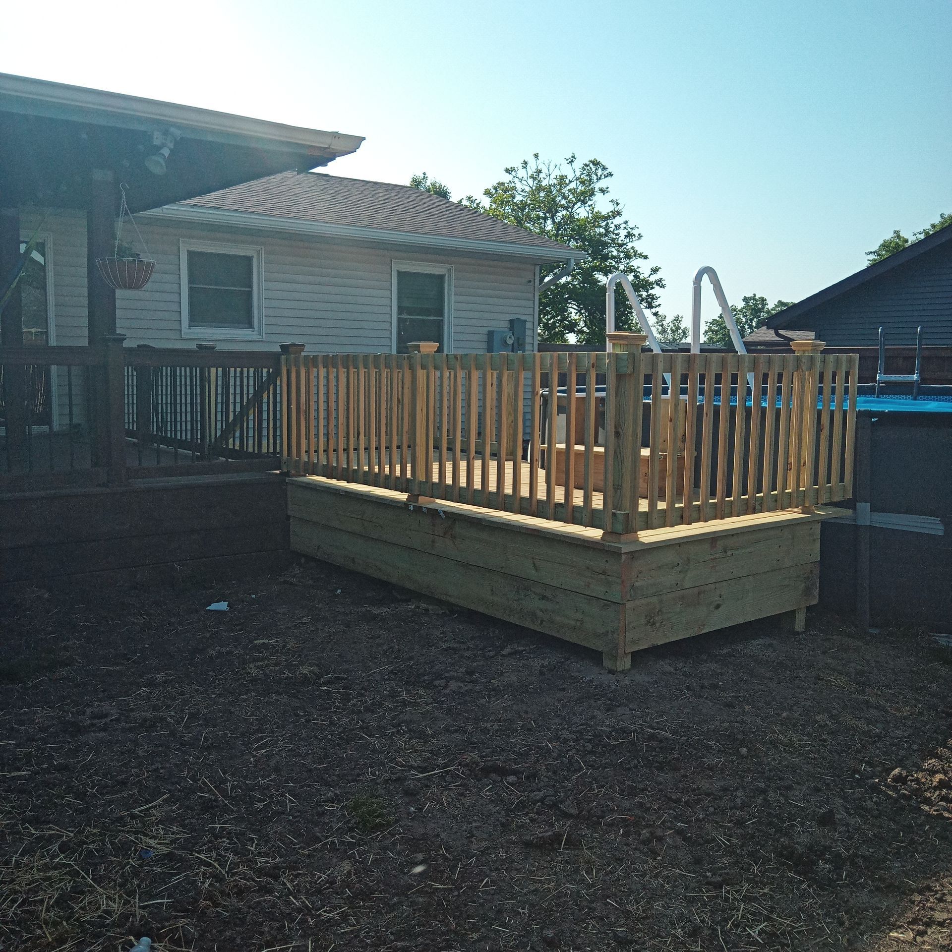 Wooden deck with a built-in above-ground pool, surrounded by a wooden railing, in a yard.