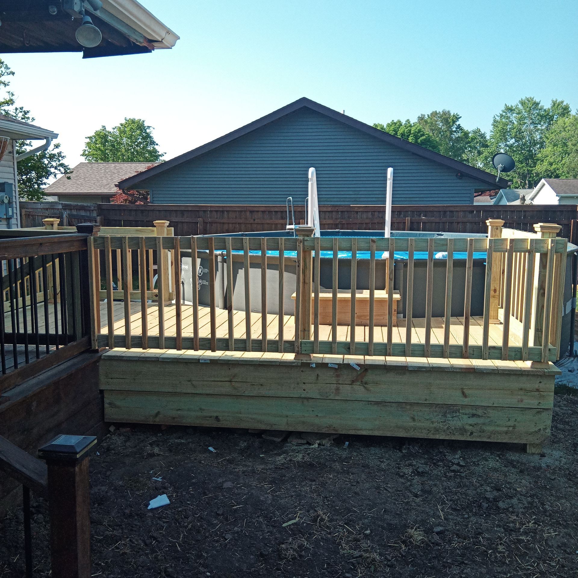 Above ground pool with wooden deck and railing in a backyard.