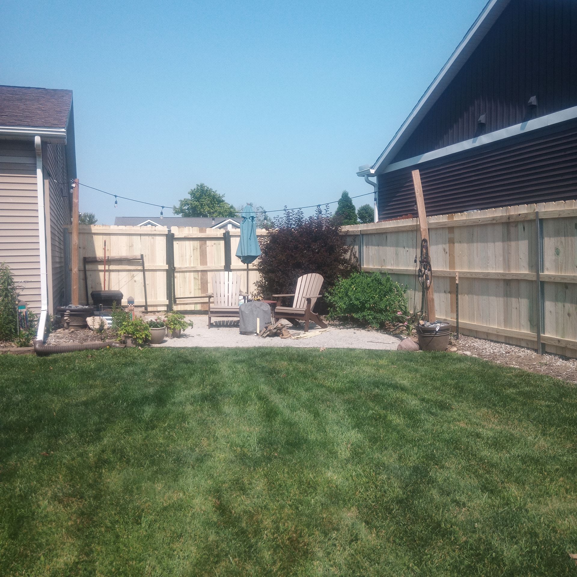 Backyard with wooden fence, patio area, two chairs, and string lights.