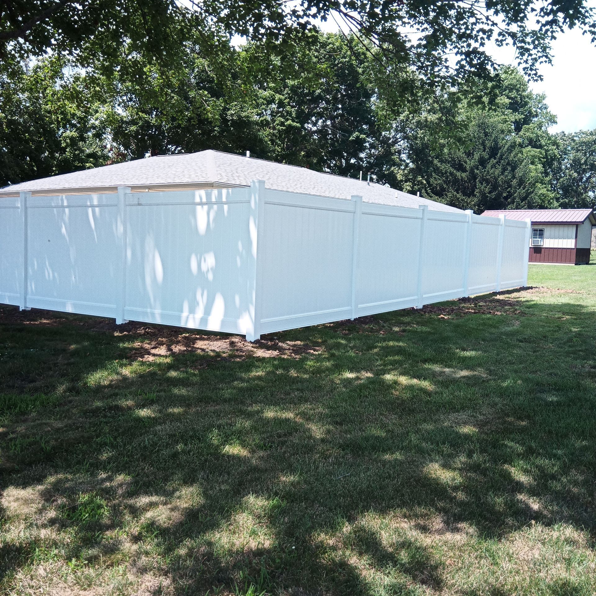 White vinyl fence surrounding a structure with a white roof on a grassy lawn with trees in the background.