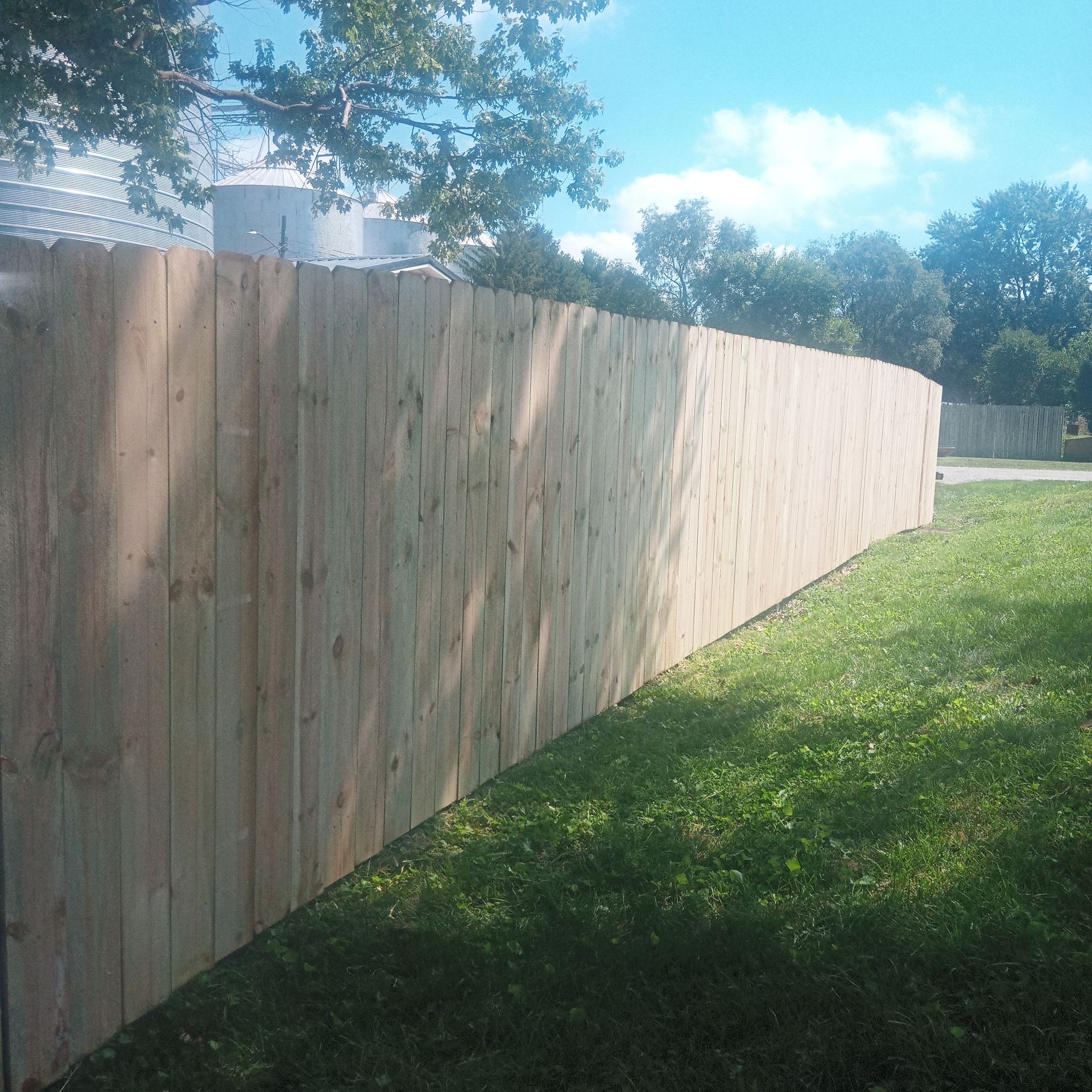 Wooden privacy fence in front of a green grassy lawn, under a partly cloudy sky.