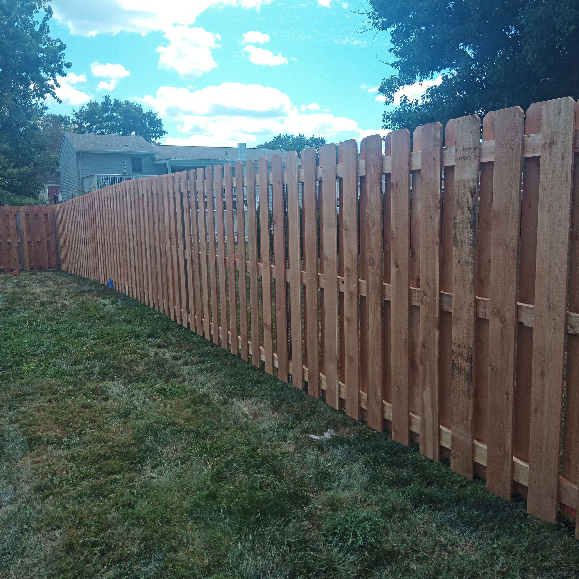 Wooden fence in a backyard with green grass and a house in the background.