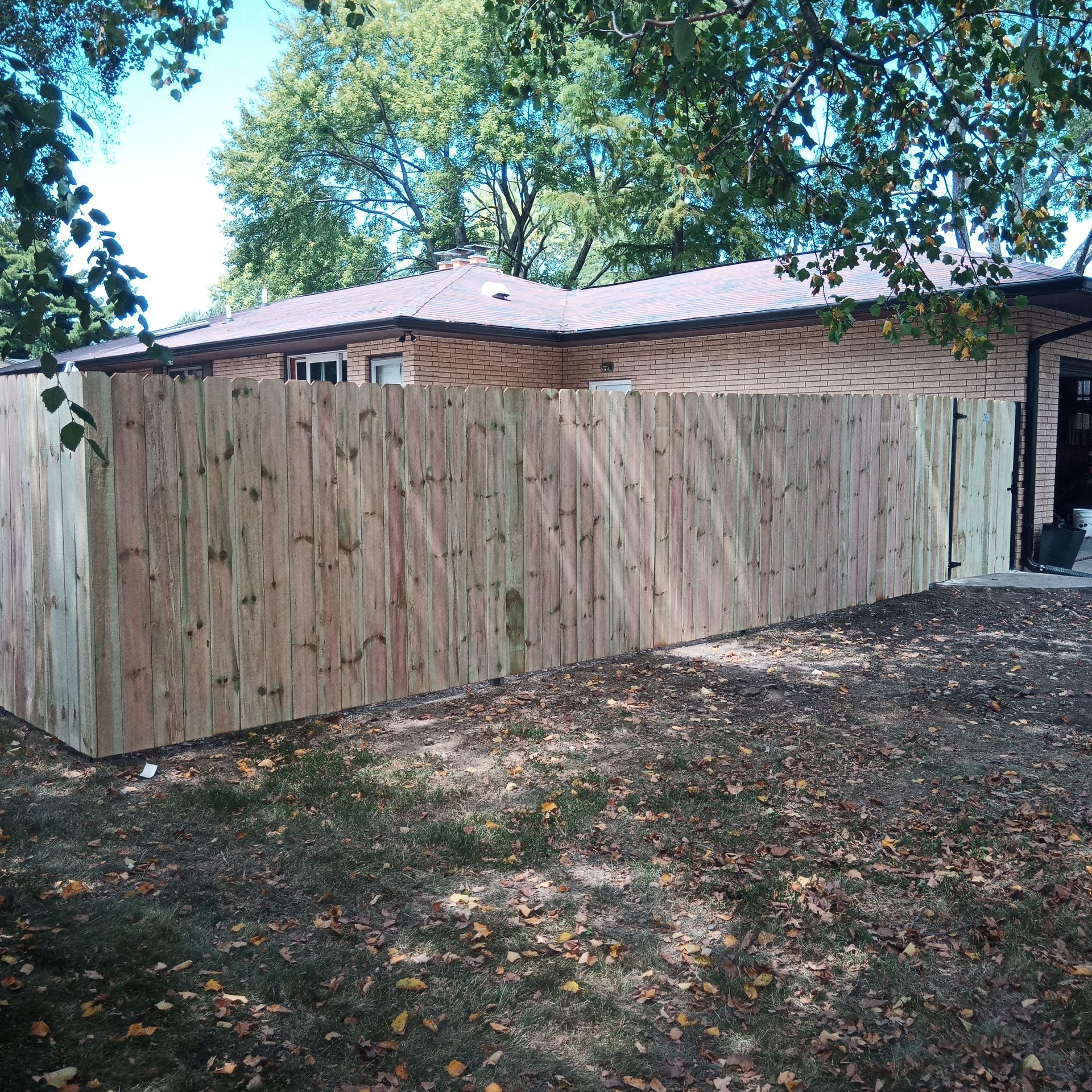 Wooden fence surrounding a brown-roofed house on a sunny day.