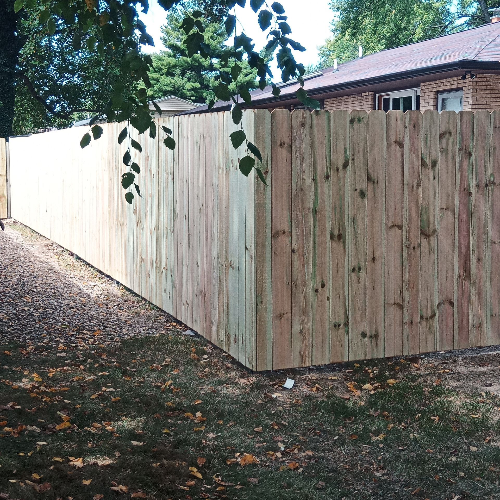 Wooden fence in a yard with leaves and a house visible in the background.
