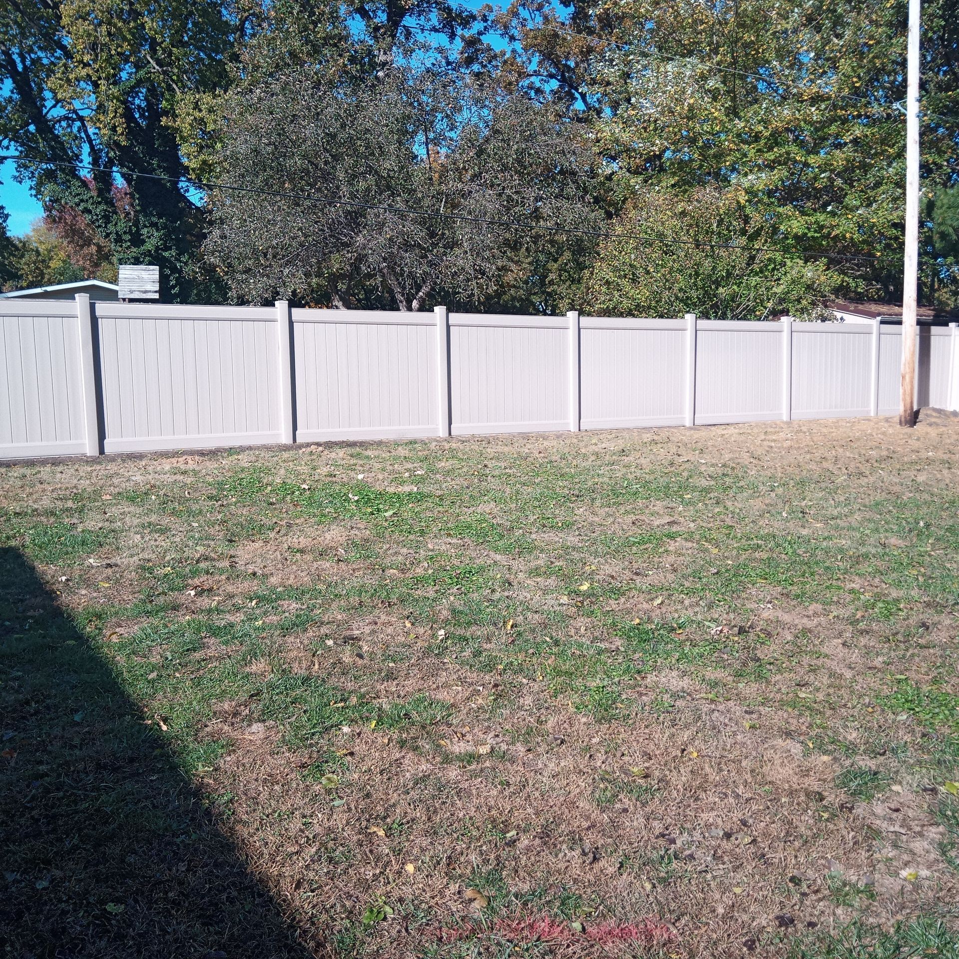 White vinyl fence enclosing a grassy backyard under a blue sky with trees in the background.