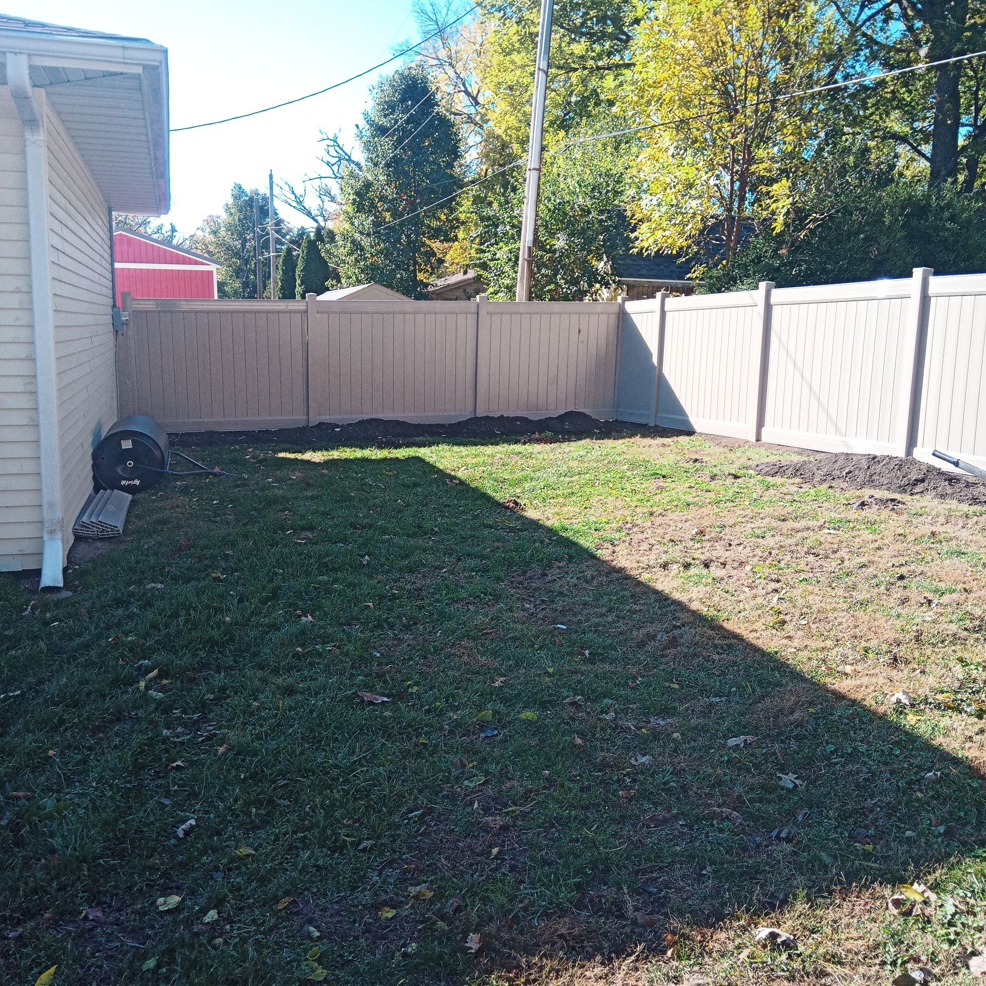 Backyard with a brown fence, green grass, and a beige house.