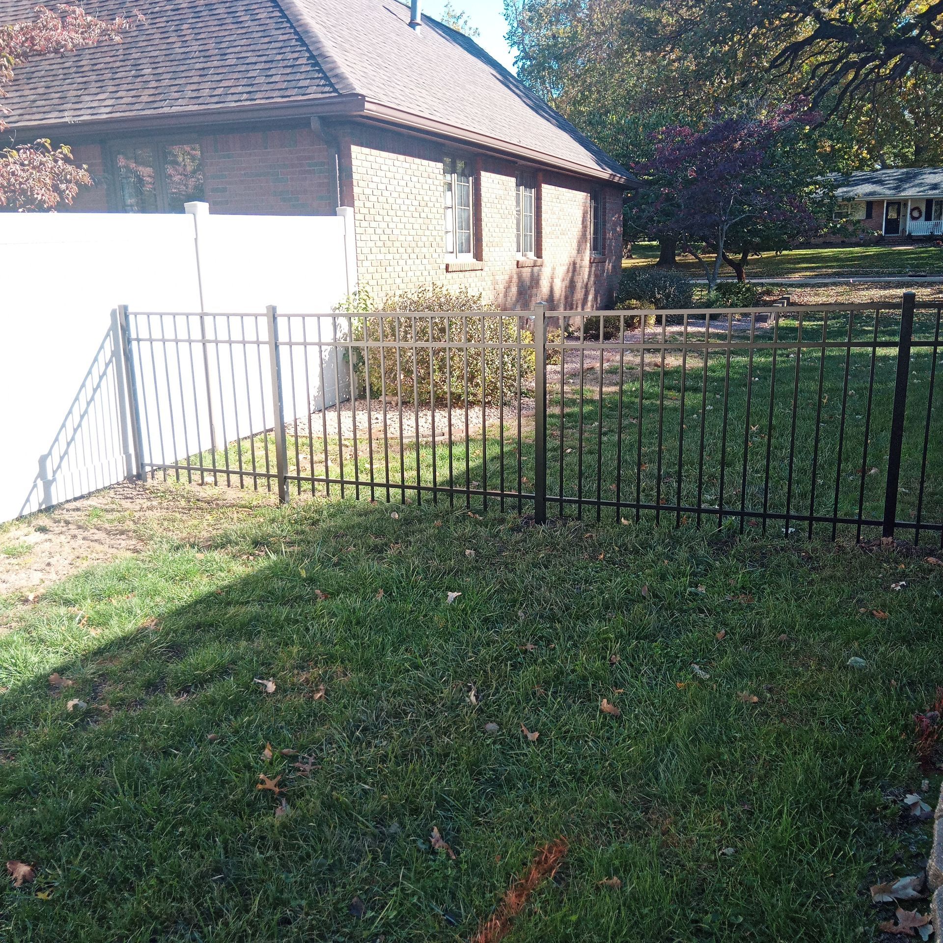 Black metal fence and white privacy fence around a brick building with grass.