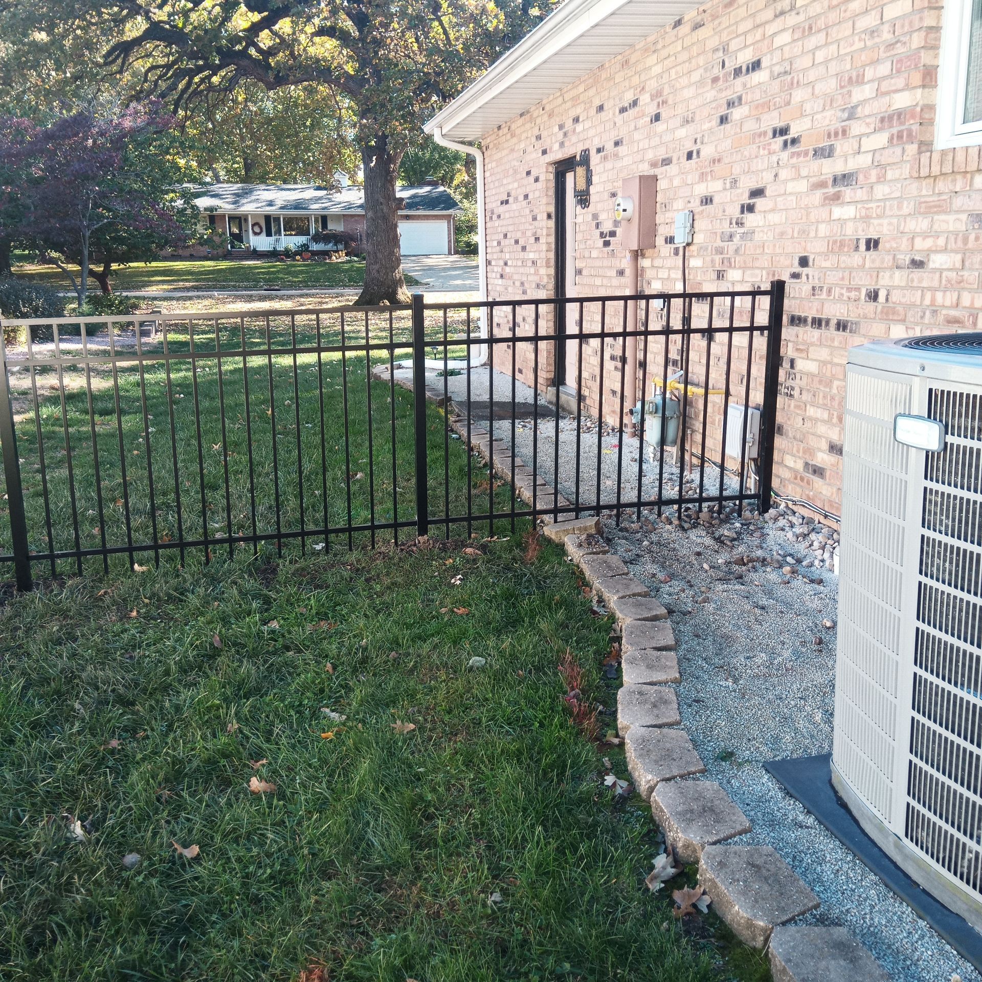 Black metal fence around a yard with grass, a brick house, and an AC unit.