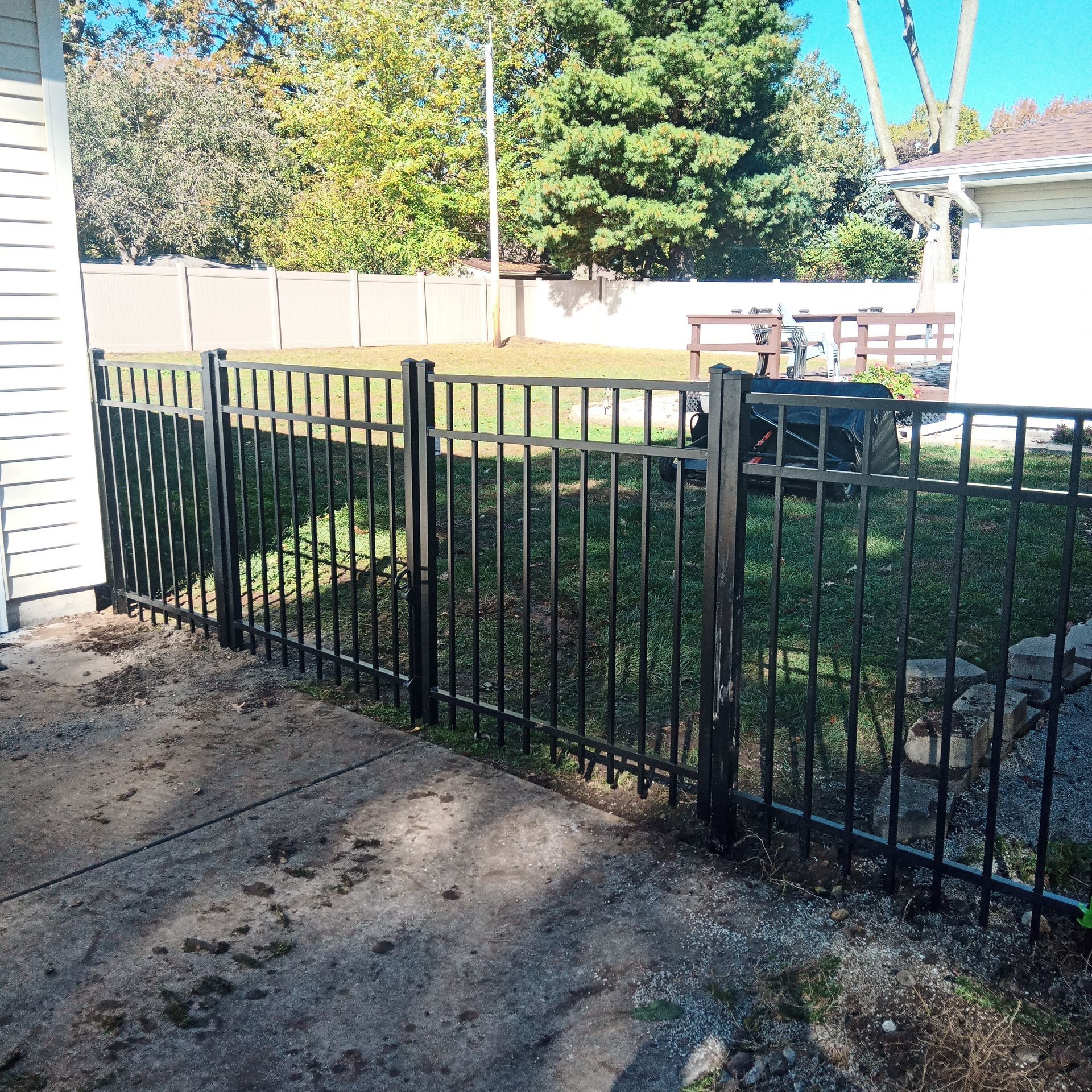 Black metal fence in a yard, separating a patio from a grassy area.