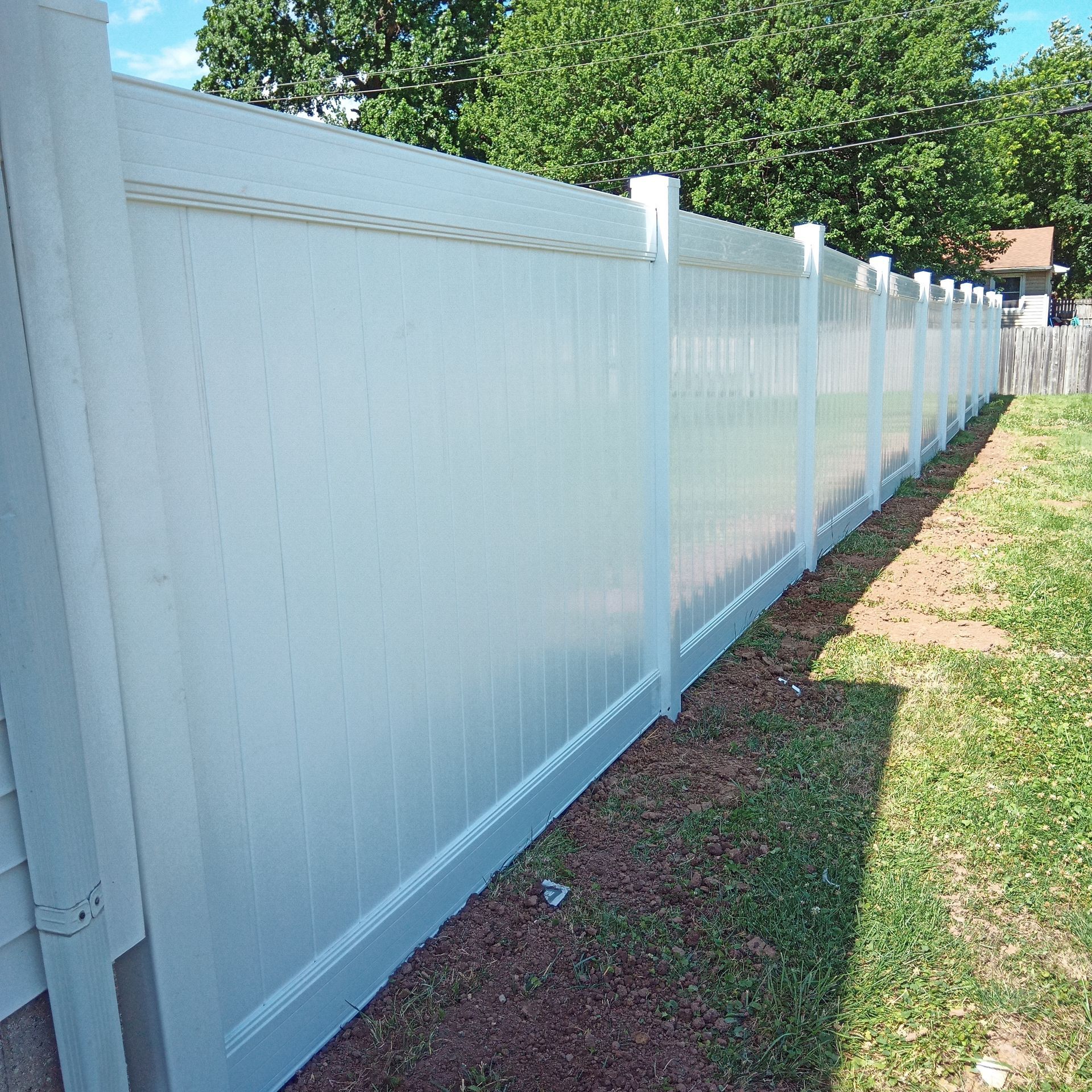 White vinyl fence in a grassy yard, sunlight casts long shadows.