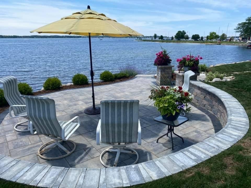 Patio with chairs, umbrella, and potted flowers overlooking a body of water.