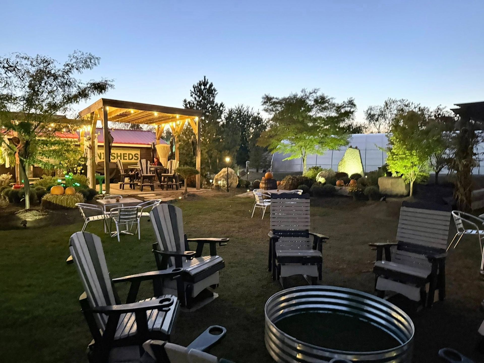 Outdoor seating area with fire pit, chairs, tables, and string lights at dusk.