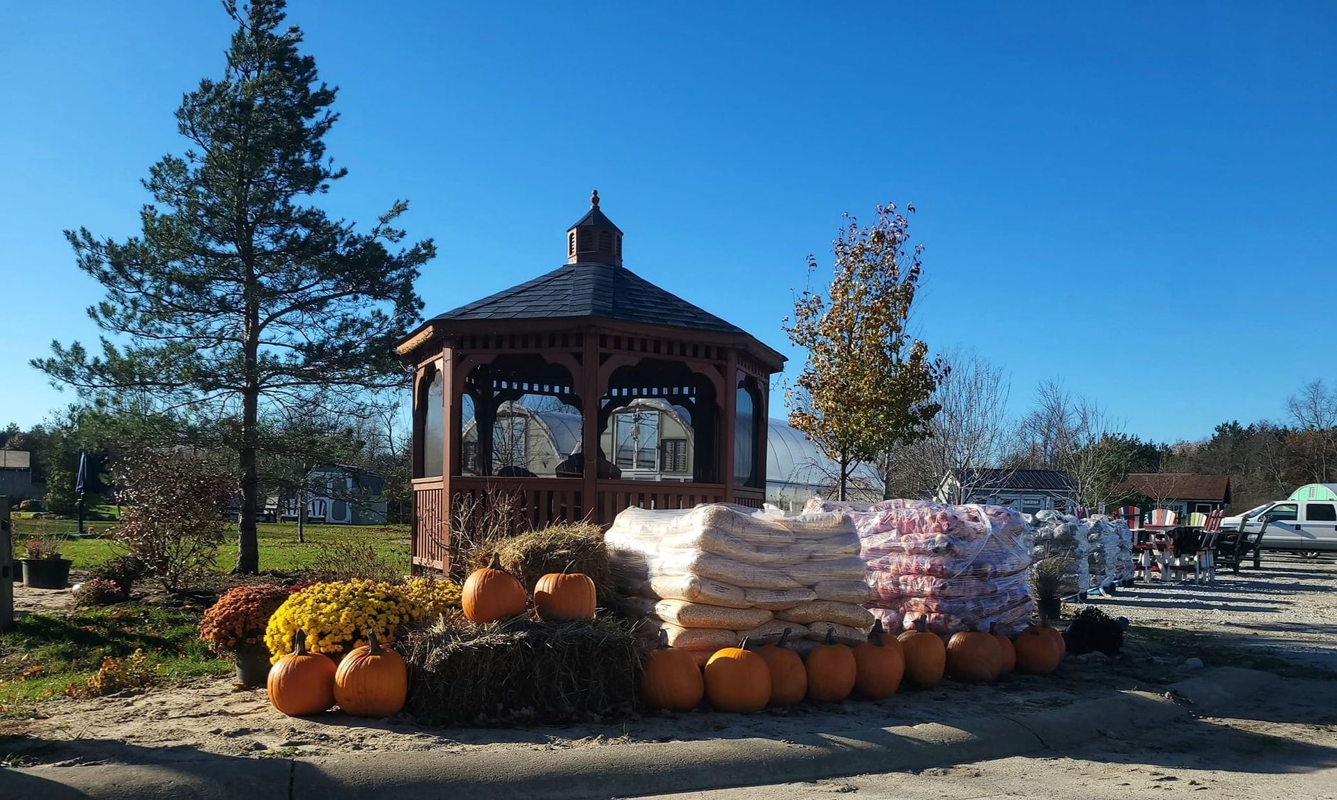 A gazebo with pumpkins and mums in front, with bags of product displayed on a sunny day.