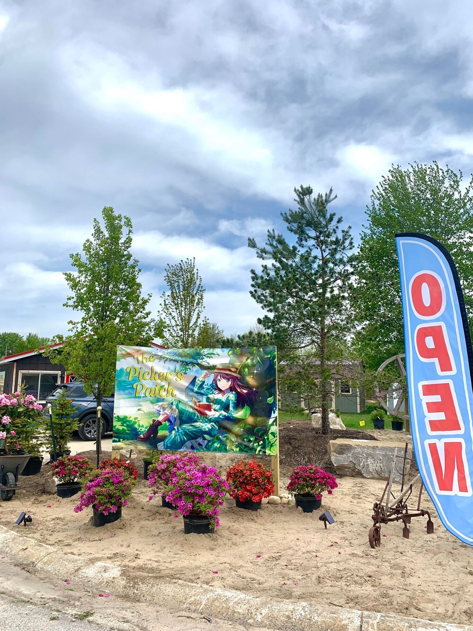 Flower shop exterior with colorful potted plants, open sign, and a painting under a cloudy sky.