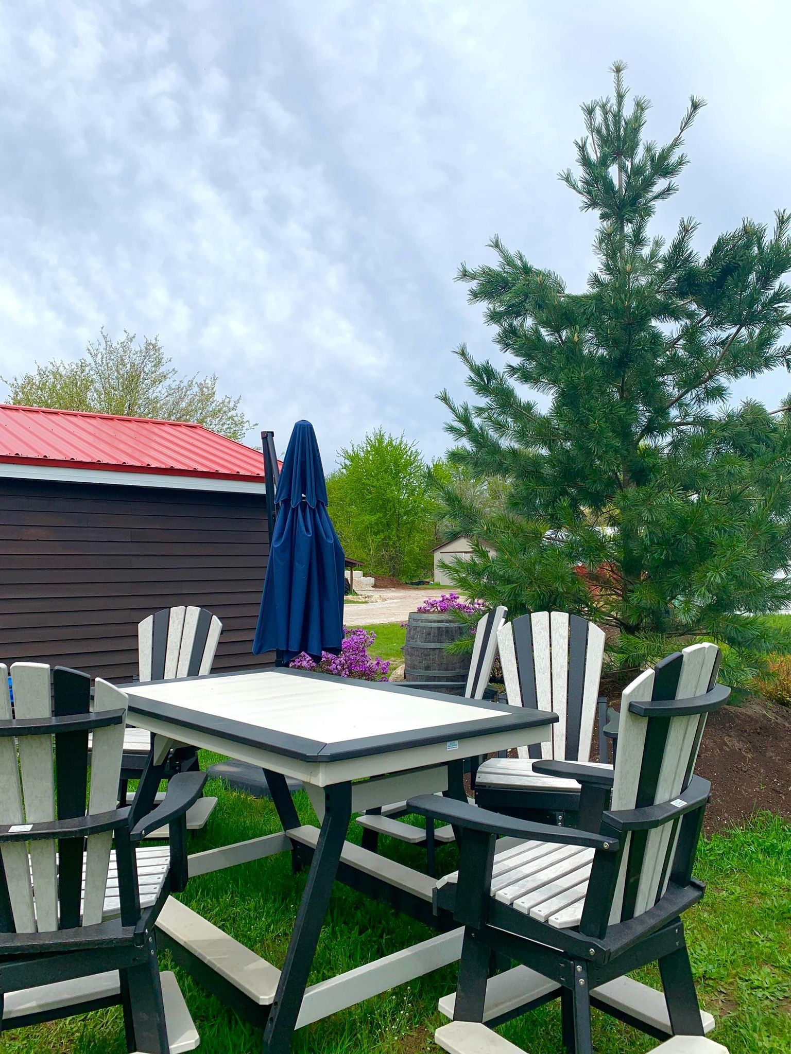 Patio set with striped chairs, umbrella, and a small building with a red roof on a grassy area under a cloudy sky.