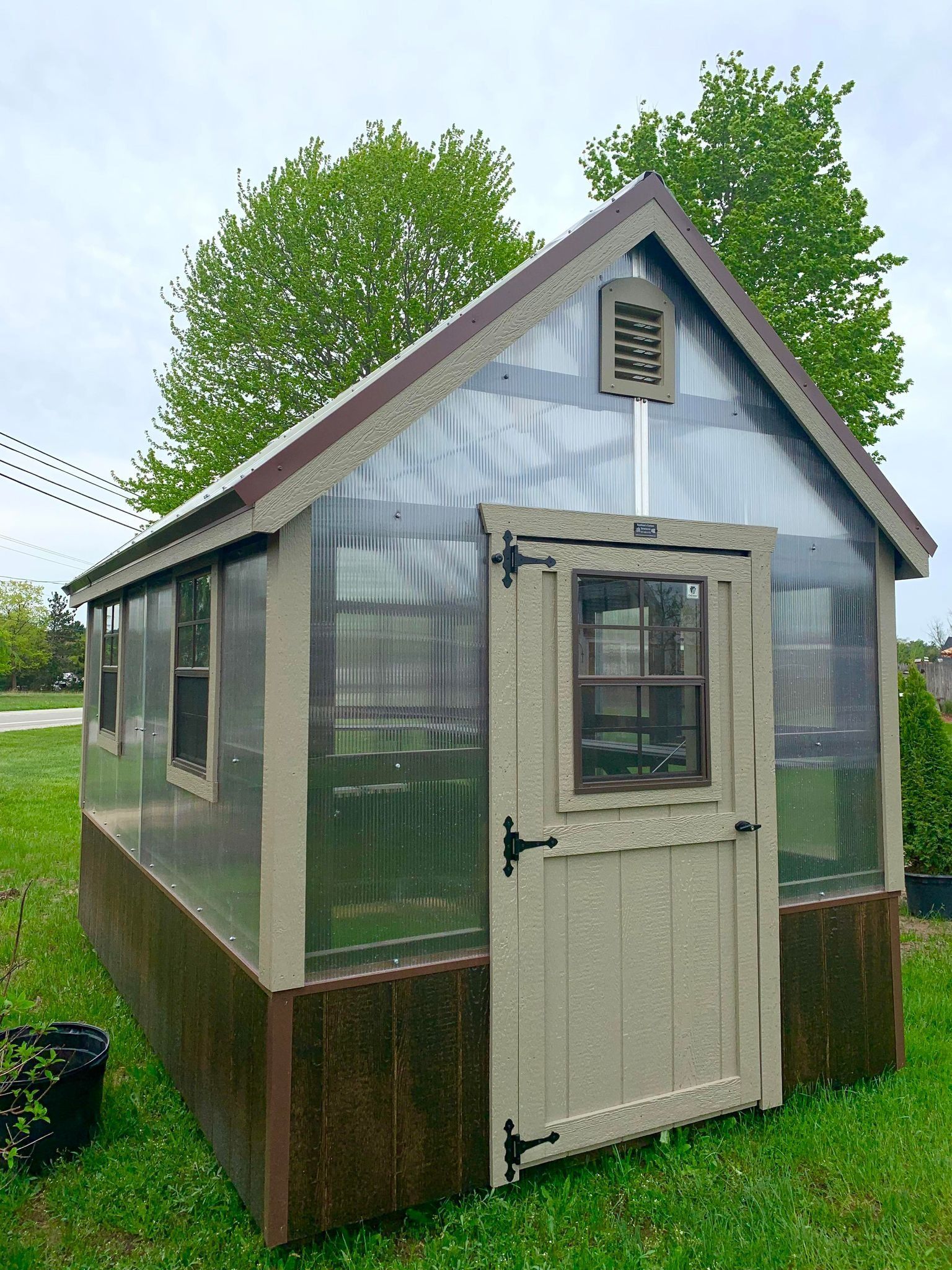 Small greenhouse with clear walls and a brown door, on a grassy lawn.