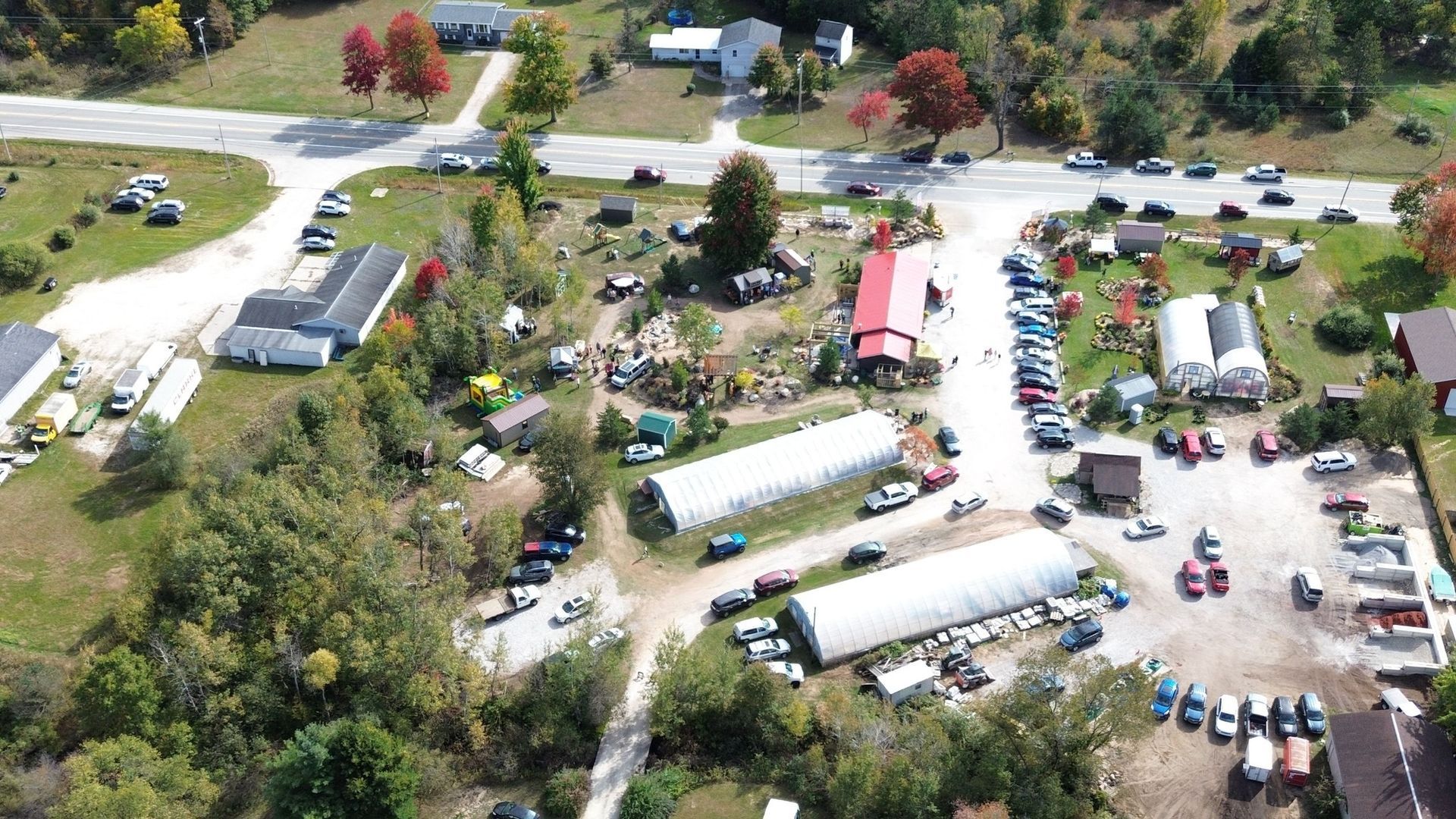 Aerial view of a roadside business with buildings, parked cars, and trees in autumn.