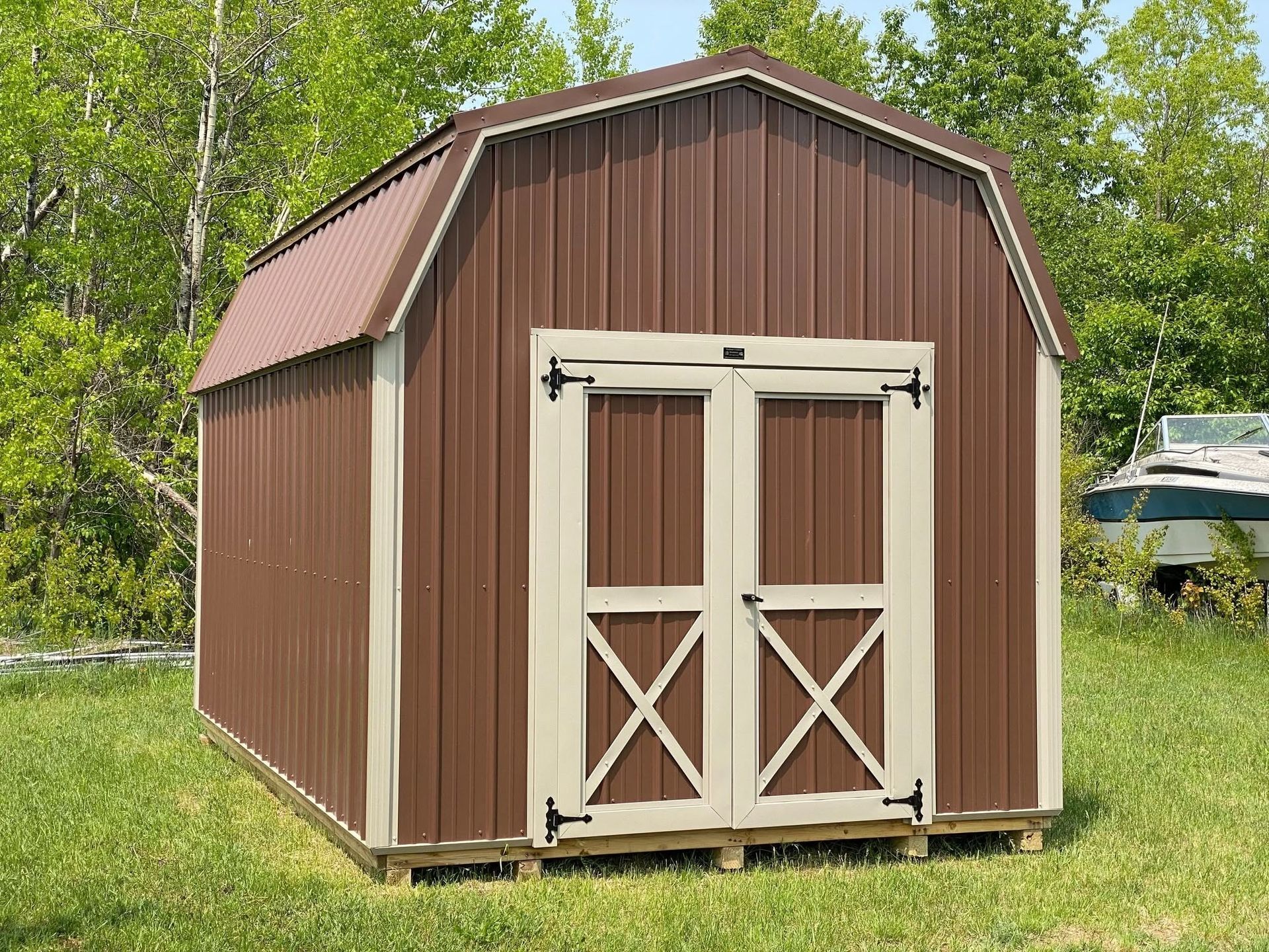 Brown metal barn shed with double doors, set in a grassy yard.