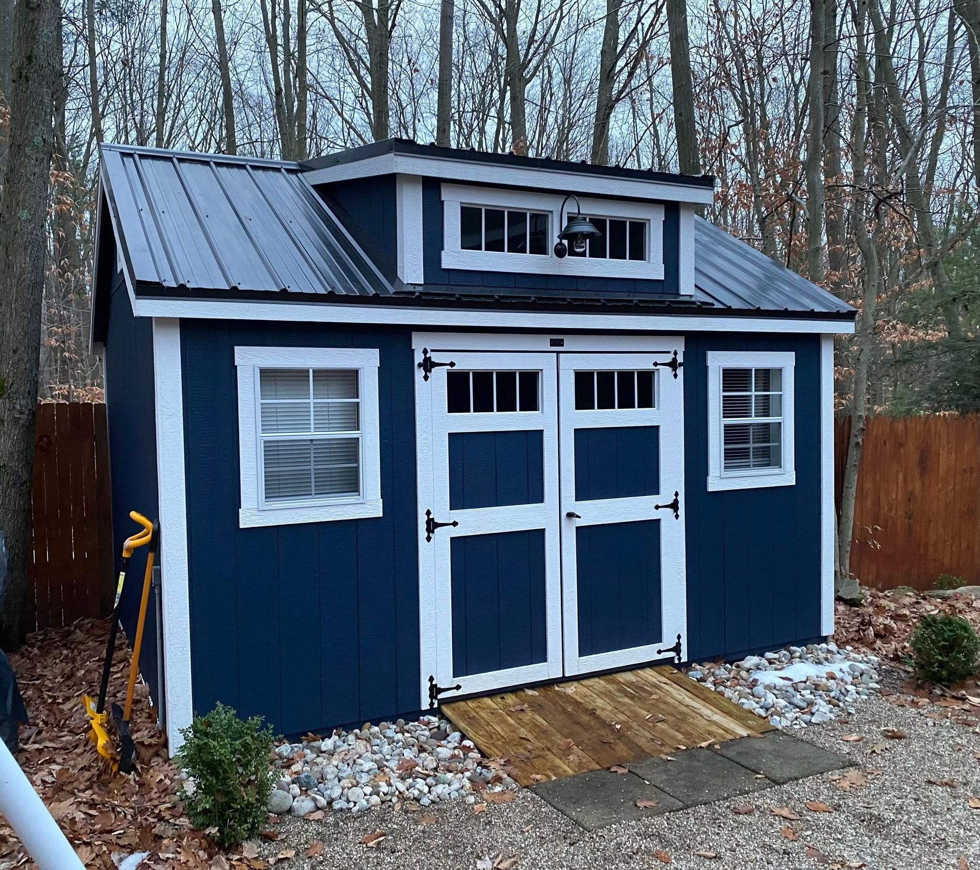 Blue shed with white trim, black metal roof, and wooden ramp.