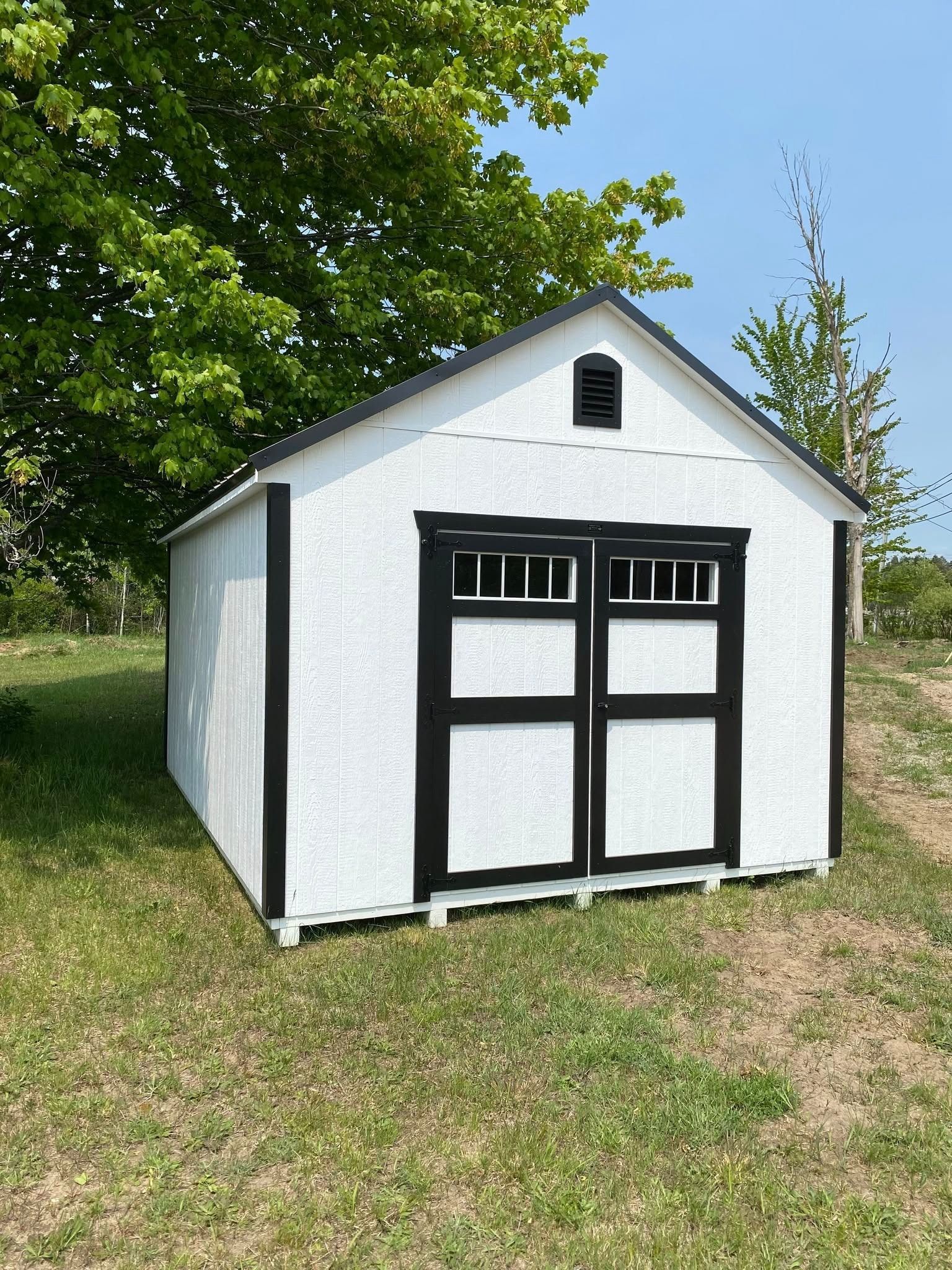 White shed with black trim and double doors on green grass.