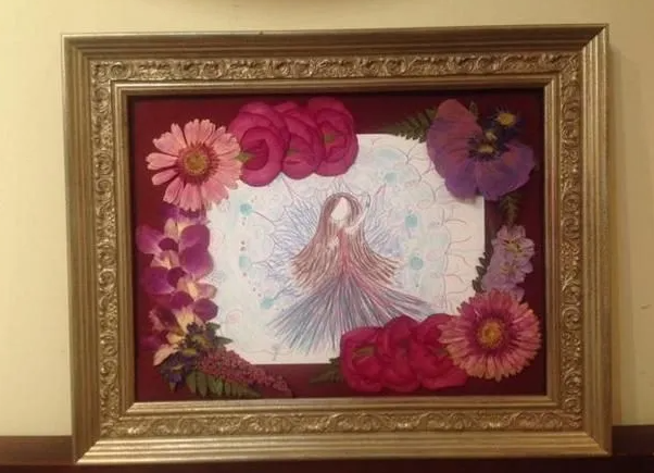 Framed artwork with a drawing of a woman surrounded by pressed flowers on a red background.