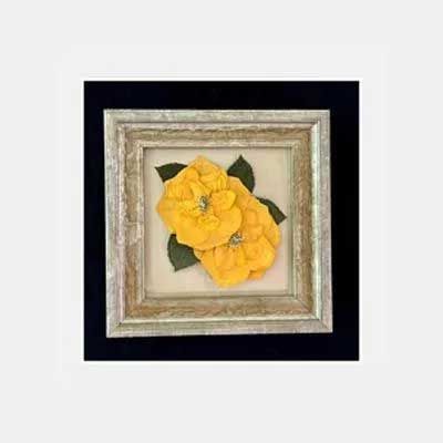 Framed pressed yellow flowers, set against a light background. Framed in a light silver frame, on a black background.