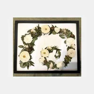 Floral arrangement in a spiral shape, framed. Features white roses and green foliage on white background.