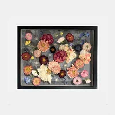 Black framed shadow box art with colorful dried flowers and fairy lights on a gray background.