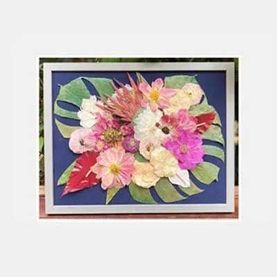Pressed flower art in a frame: colorful blooms and leaves on a blue background.