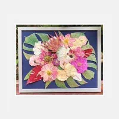 Pressed flowers in a frame with blue background; various pink, red, and yellow blooms and green leaves.