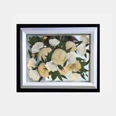 Framed floral artwork: pressed white and yellow flowers with green leaves in a black and white frame.