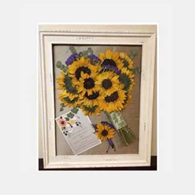 Sunflowers in a framed display with a greeting card and a small sunflower pinned below.
