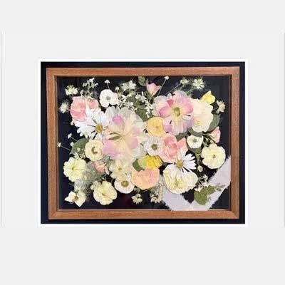 Framed floral art with pressed flowers in pink, yellow, and white against a black background.